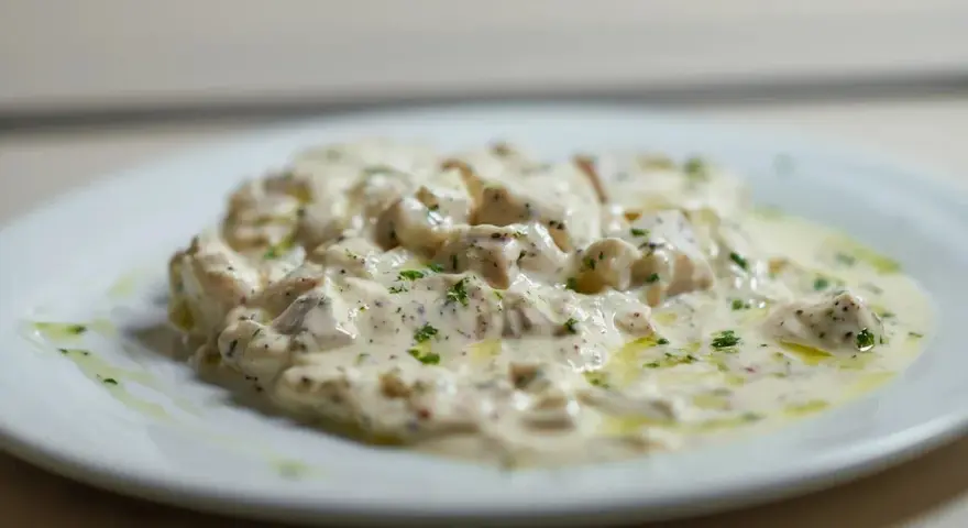 Deliciosa brandada de bacalao cremosa, con trozos de pescado blanco y perejil picado, servida en un plato blanco.