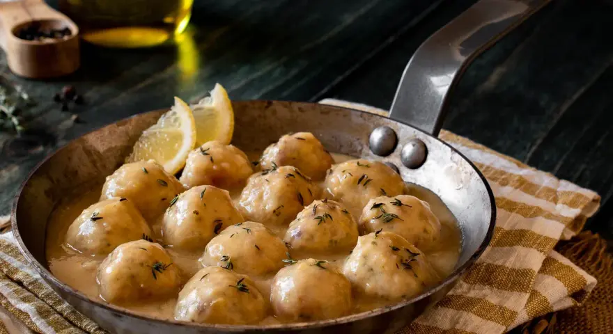 Albondigas de pollo caseras en salsa cremosa, servidas en sartén con limón y hierbas.