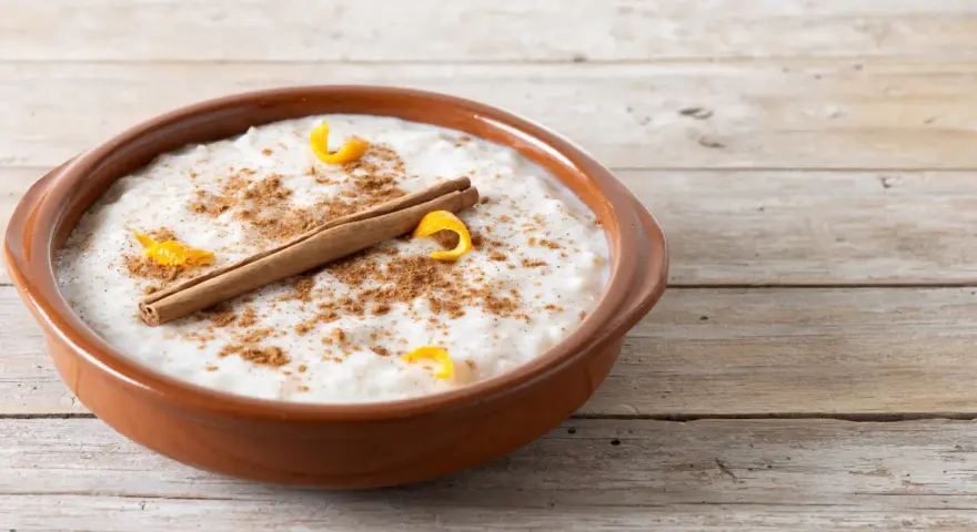 Un tazón de arroz con leche cremoso, espolvoreado con canela y adornado con cáscara de naranja y una rama de canela.
