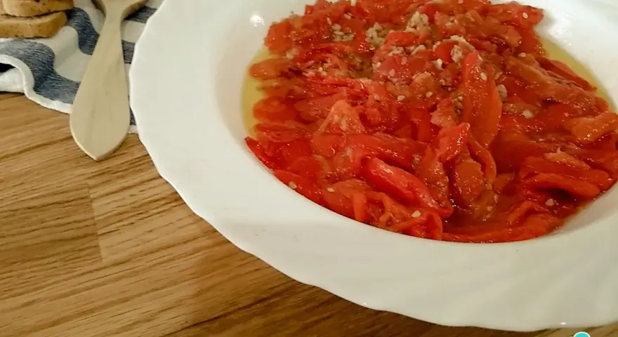 Asadillo manchego, pimientos asados con ajo y aceite, listos para disfrutar con tostadas y una cuchara de madera.
