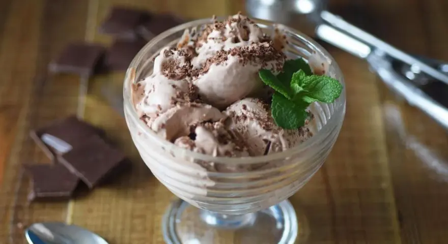 Delicioso helado de chocolate con virutas de chocolate y una hoja de menta, servido en copa de cristal.