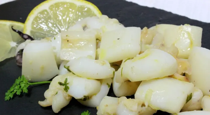 Sabrosa sepia al ajillo, troceada y salteada con ajo y perejil, servida con rodajas de limón.