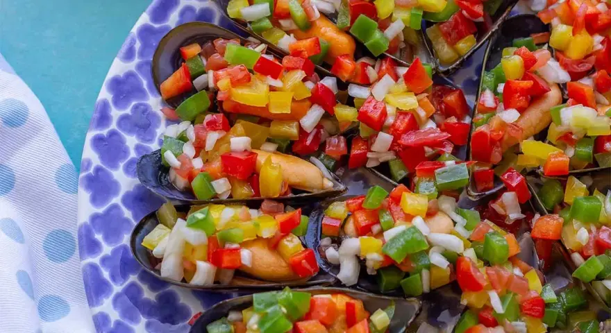Mejillones a la vinagreta, cubiertos con una colorida mezcla de pimientos picados y cebolla.