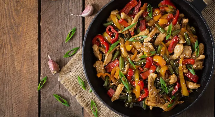 Sabroso wok de pollo con pimientos de colores y judías verdes, espolvoreado con semillas de sésamo y cebolleta.