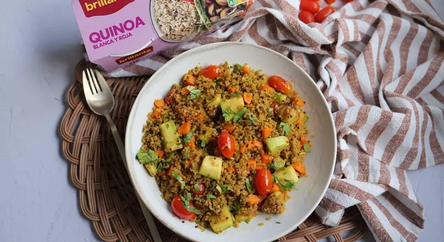 Un plato de quinoa con verduras, incluyendo tomates cherry, calabacín y zanahoria, listo para disfrutar.