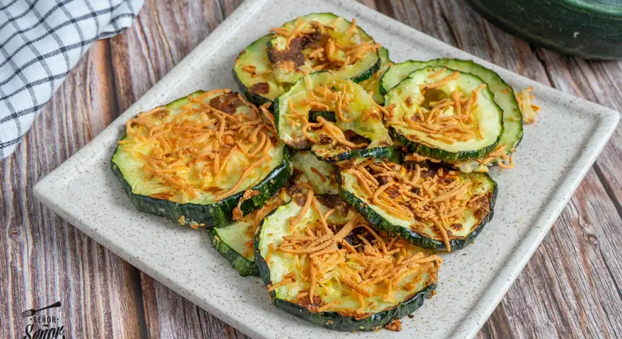 Rodajas de calabacín en freidora de aire, doradas y crujientes, con un toque de queso rallado. ¡Una delicia saludable!