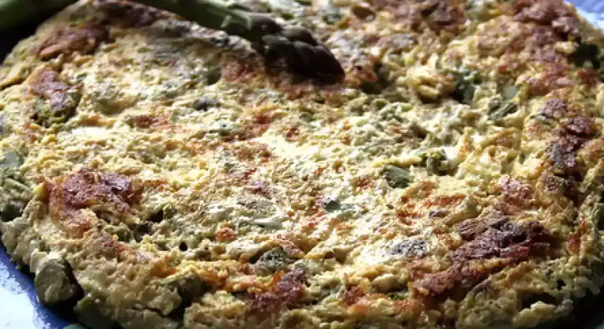 Tortilla de esparragos dorada y esponjosa, con espárragos frescos encima, servida en un plato azul.