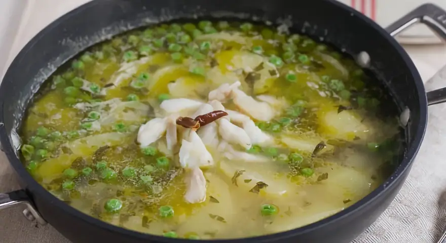 Patatas en salsa verde con trozos de pescado blanco y guisantes, servido en una sartén.