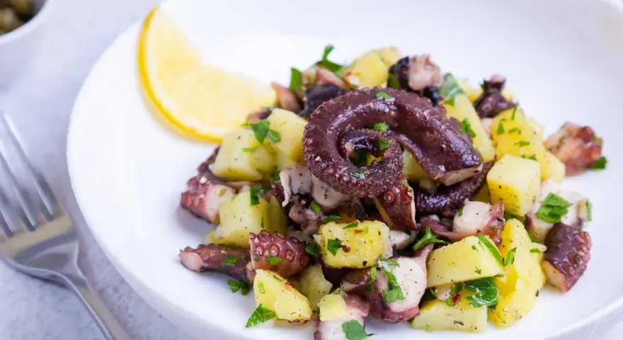 Ensalada de pulpo y patatas, un ejemplo de recetas sanas con pulpo. Servida en plato blanco con limón y perejil.