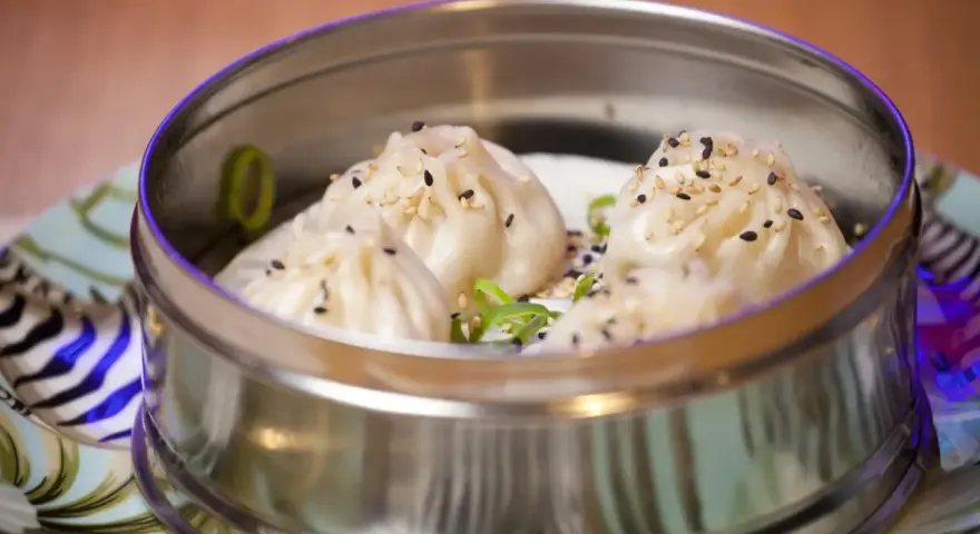 Deliciosos dumplings al vapor, cubiertos con semillas de sésamo y cebolleta, servidos en una vaporera metálica.
