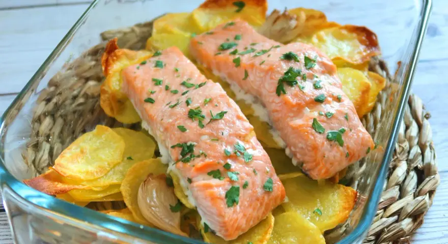 Dos filetes de salmón al horno con patatas crujientes y perejil picado, servidos en una fuente de vidrio.