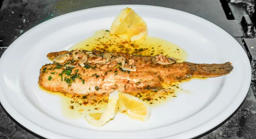 Delicioso lenguado a la meunière, bañado en mantequilla dorada, ajo y perejil, con gajos de limón.