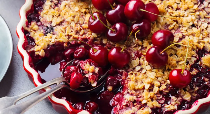 Delicioso postre con cerezas, cubierto de crumble dorado y adornado con cerezas frescas.