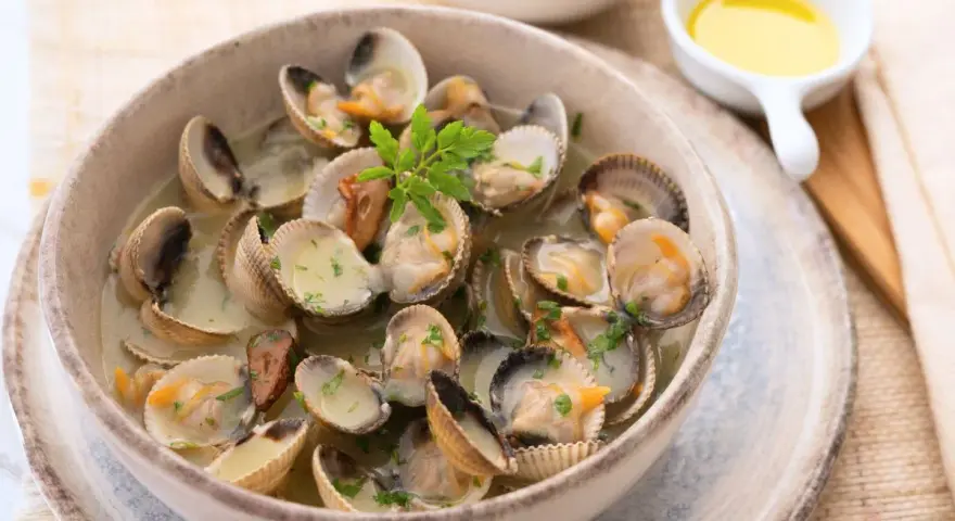 Deliciosos tipos de berberechos cocinados en su jugo, servidos en un cuenco de cerámica con perejil picado.