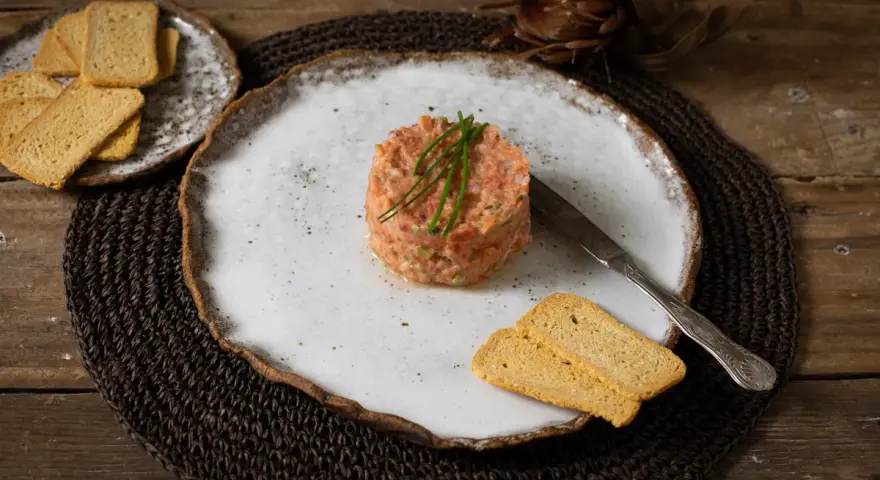 Delicioso tartar de tomate, servido con tostas crujientes y un cuchillo de plata. Un plato fresco y vibrante.