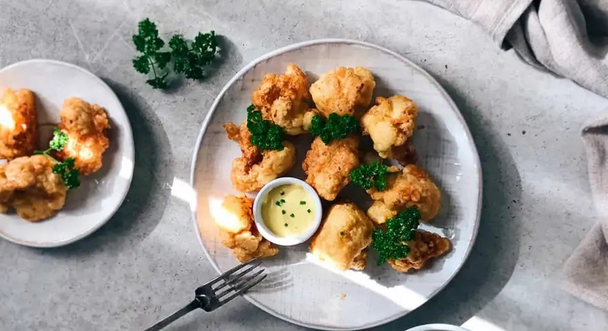 Crujientes trozos de coliflor rebozada, servidos con una cremosa salsa y decorados con perejil fresco. ¡Un aperitivo delicioso!