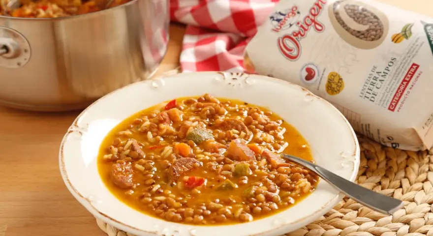Plato de lentejas con arroz, chorizo y verduras. Una bolsa de lentejas "Origen" a un lado.