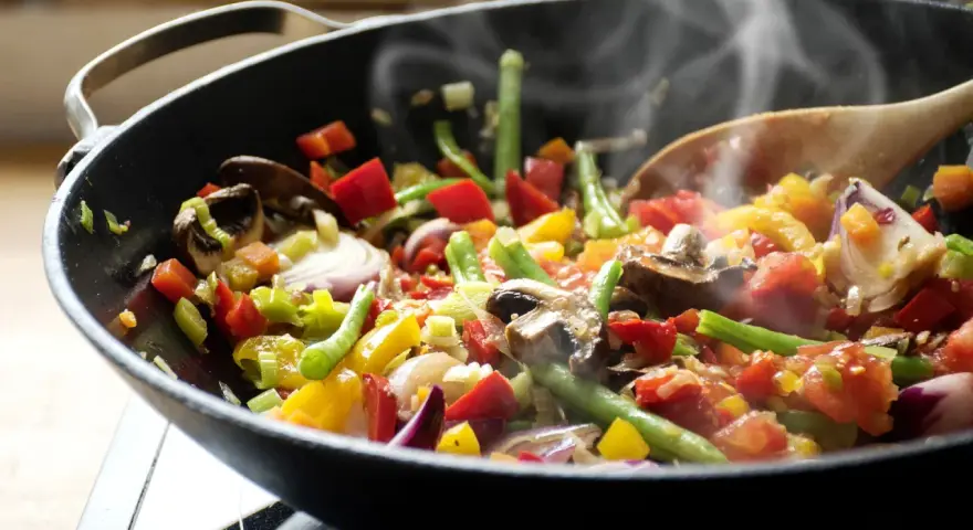 Un delicioso salteado de verduras humeante en un wok, con pimientos, judías verdes, champiñones y cebolla morada.