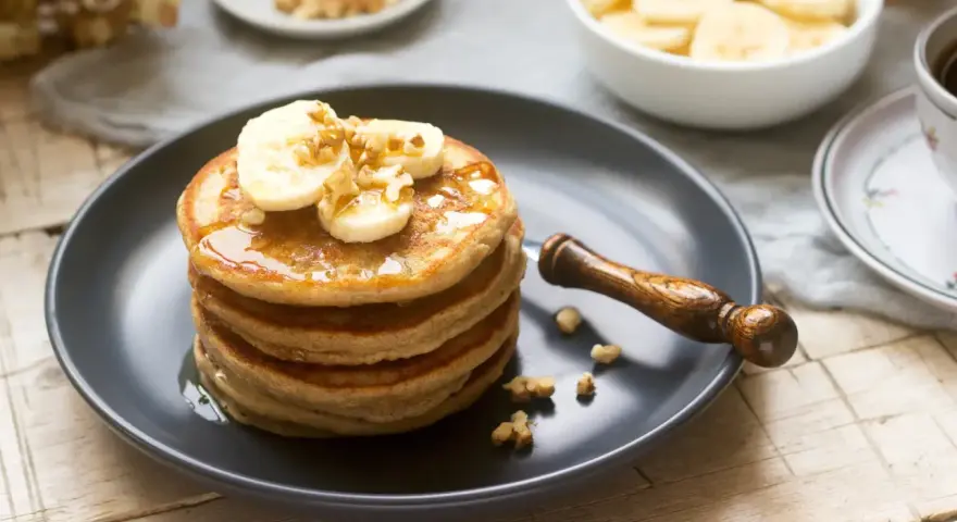 Pila de tortitas americanas con plátano, nueces y sirope. Un desayuno delicioso y nutritivo.