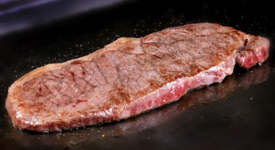 Un jugoso filete de ternera, perfectamente cocinado, chisporrotea en la plancha, listo para ser disfrutado.