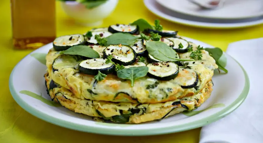 Deliciosa tortilla de calabacín y espinacas, coronada con rodajas de calabacín y hierbas frescas.
