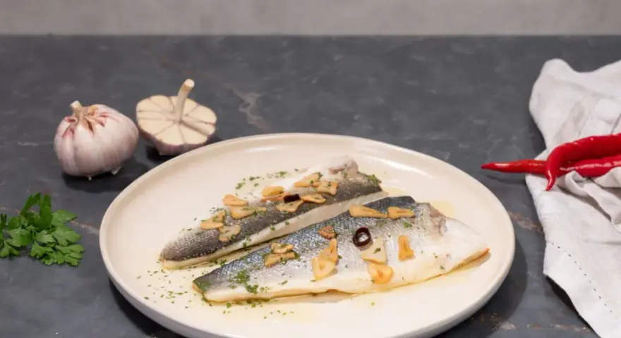 Dos filetes de lubina a la donostiarra, con láminas de ajo dorado, perejil picado y un toque de guindilla.