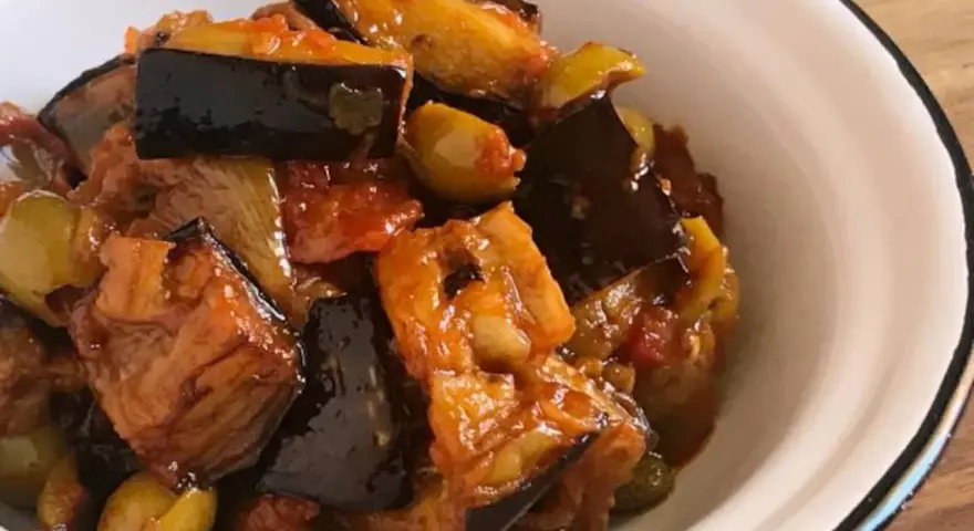 Un plato de caponata siciliana, con berenjenas, aceitunas y tomate, servido en un cuenco blanco.