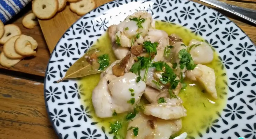 Plato de que son las cocochas de bacalao, tiernas y jugosas, en una salsa amarilla con perejil picado y galletas tostadas al lado.