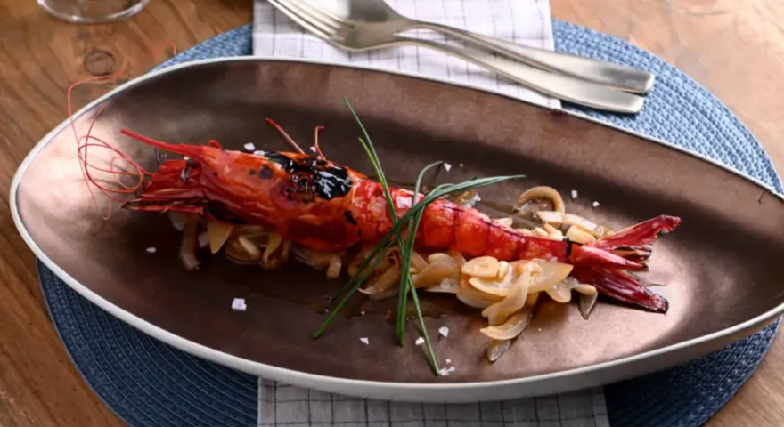 Un langostino rojo a la parrilla, servido sobre cebolla caramelizada y adornado con cebollino. Un plato que evoca la pregunta: ¿qué son los carabineros?