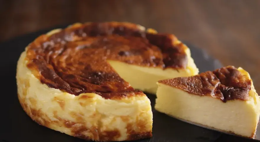 Tarta de queso al horno casera, dorada y cremosa, con una porción lista para disfrutar.