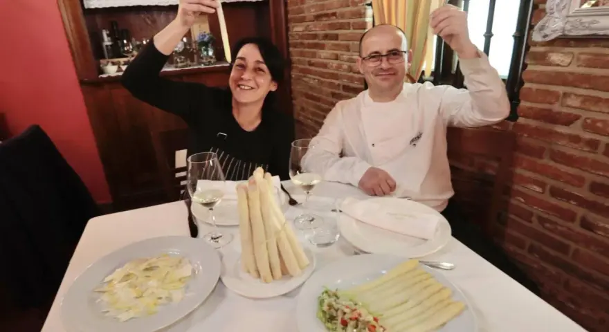 Pareja sonriente celebra con espárragos blancos en un restaurante. Platos de espárragos blancos y ensalada adornan la mesa.
