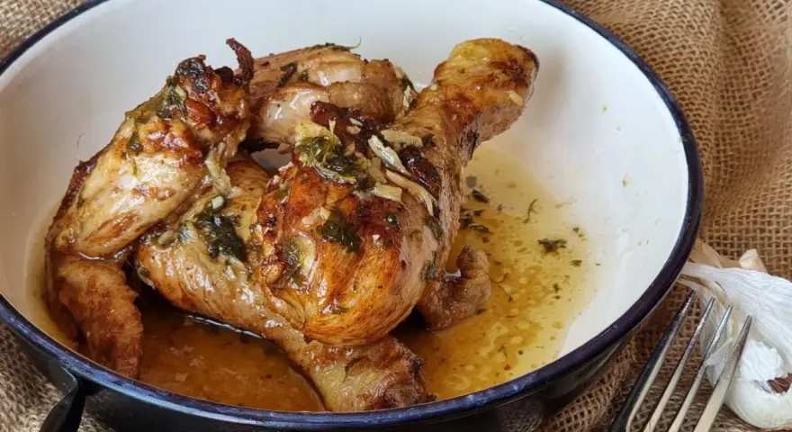 Sabroso pollo al ajillo dorado y jugoso, servido en una cazuela con su jugo y hierbas.