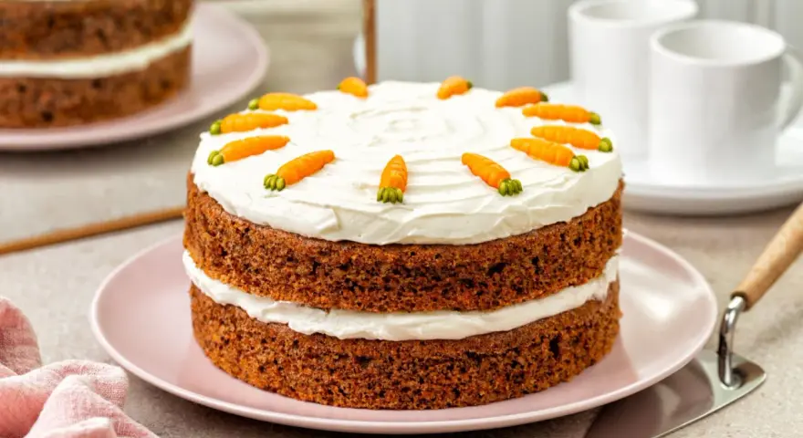 Delicioso bizcocho de zanahoria de dos pisos, cubierto con glaseado blanco y decorado con zanahorias de mazapán.