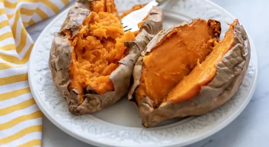 Boniato tierno y esponjoso hecho en air fryer, servido en plato blanco con un tenedor.