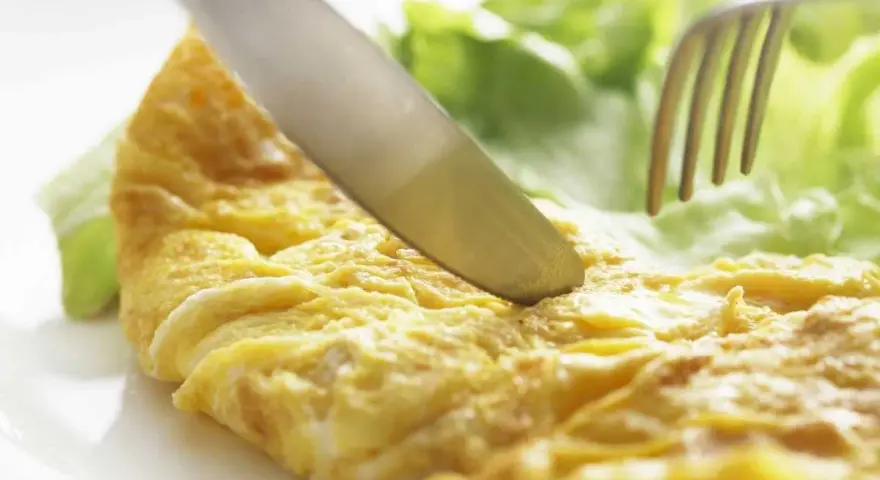 Un cuchillo corta una dorada tortilla francesa servida con hojas de lechuga fresca.