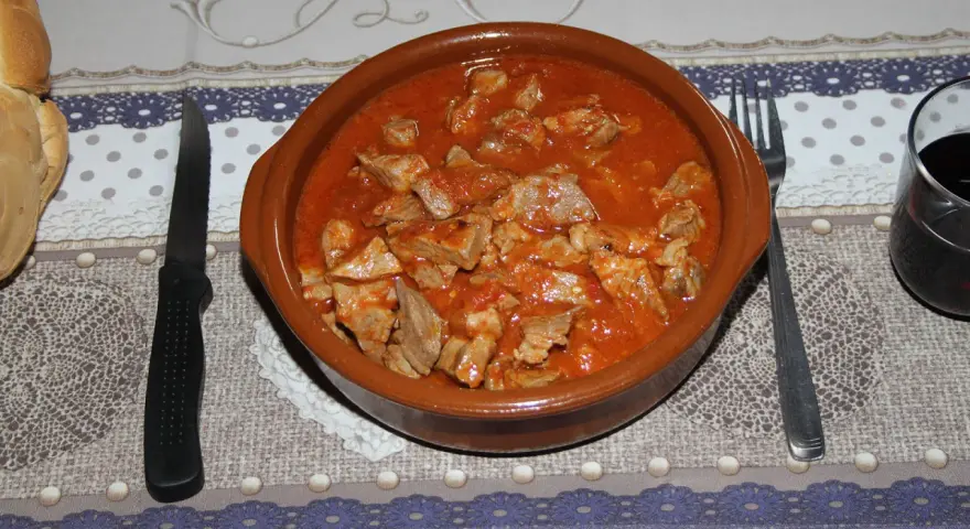 Un cuenco de barro rebosante de magro con tomate, listo para ser disfrutado con pan y vino tinto.
