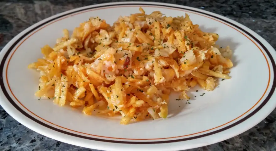 Bacalao dorado desmenuzado con patatas fritas finas y perejil picado, servido en un plato blanco con borde marrón y naranja.
