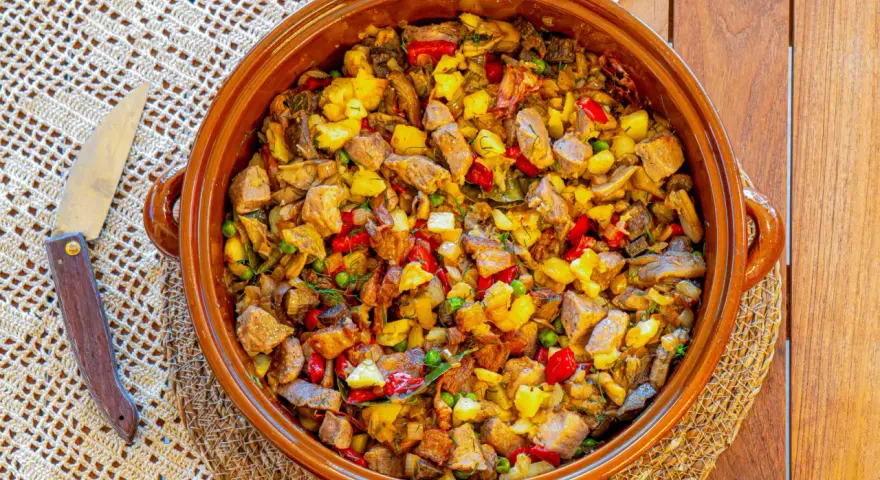 Un generoso plato de frito mallorquín, con trozos de carne, patatas, pimientos y guisantes, servido en una cazuela de barro.