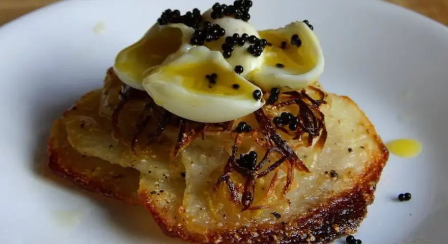 Delicioso aperitivo con patatas crujientes, cebolla frita, huevos de codorniz cocidos y caviar negro.