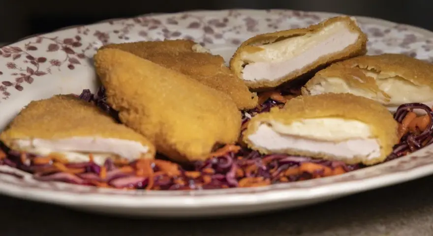 Pechuga villaroy dorada y crujiente, rellena de queso fundido, servida sobre una ensalada de col morada y zanahoria.
