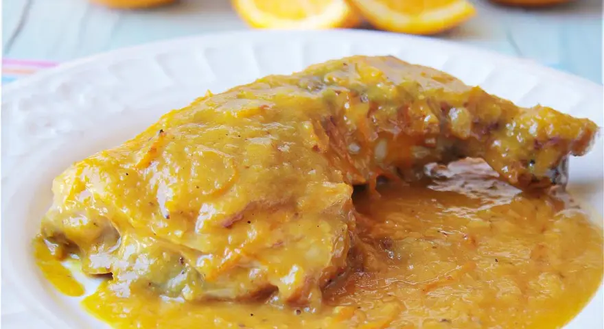Delicioso pollo a la naranja, bañado en una salsa dorada y jugosa, con gajos de naranja frescos al fondo.