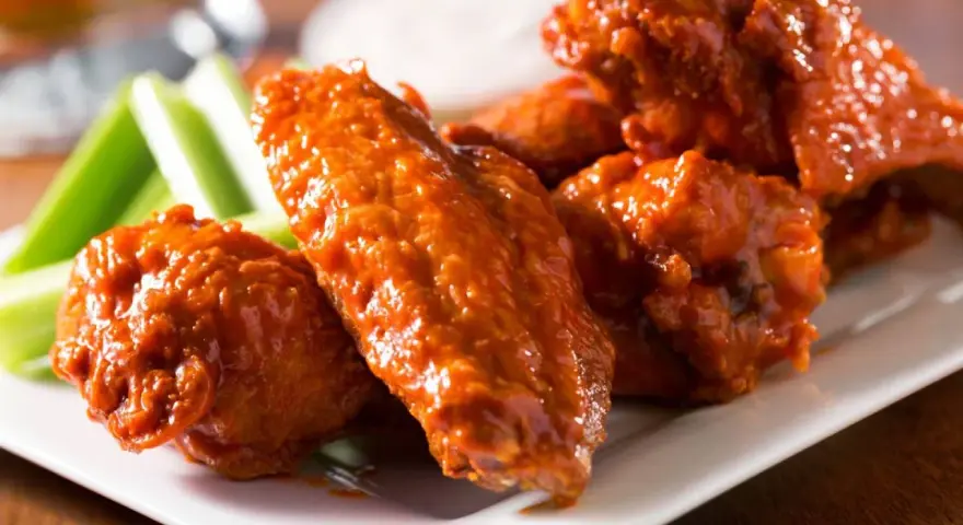 Alitas de pollo en freidora de aire, cubiertas de salsa picante, servidas con bastones de apio crujientes.