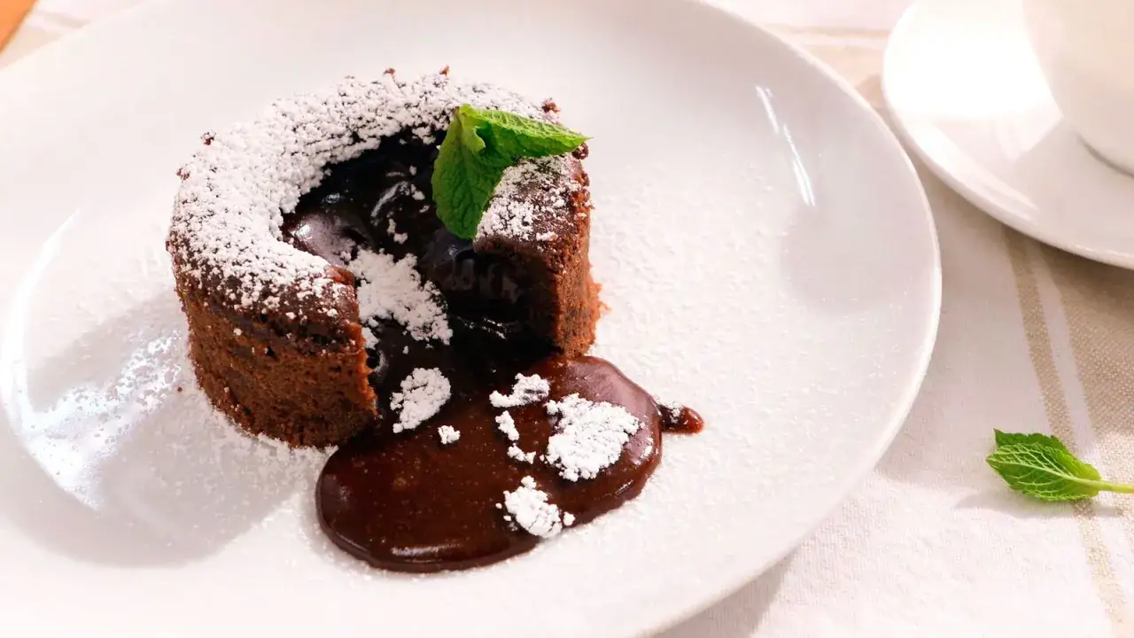 Coulant de chocolate con interior fundido, espolvoreado con az&uacute;car glas y decorado con una hoja de menta.