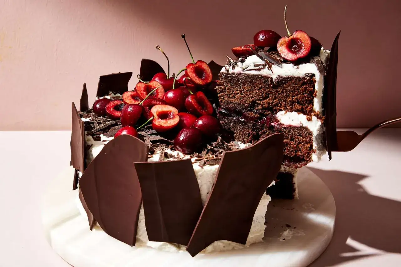 Tarta Selva Negra, con capas de bizcocho de chocolate, nata montada y cerezas frescas, decorada con virutas de chocolate y trozos de chocolate negro.
