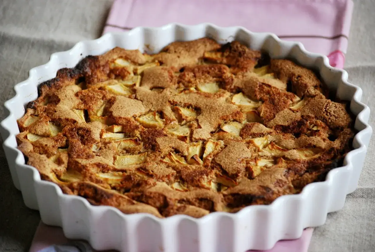 Tarta de manzana casera recién horneada, con trozos de manzana visibles bajo una cobertura dorada y crujiente.