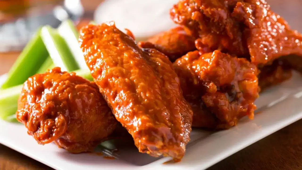 Alitas de pollo en freidora de aire, cubiertas de salsa picante, servidas con bastones de apio crujientes. ¡Un aperitivo irresistible!