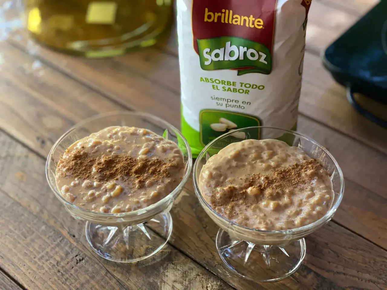 Dos copas de cremoso arroz con leche, espolvoreado con canela, junto a un paquete de arroz Sabroz.
