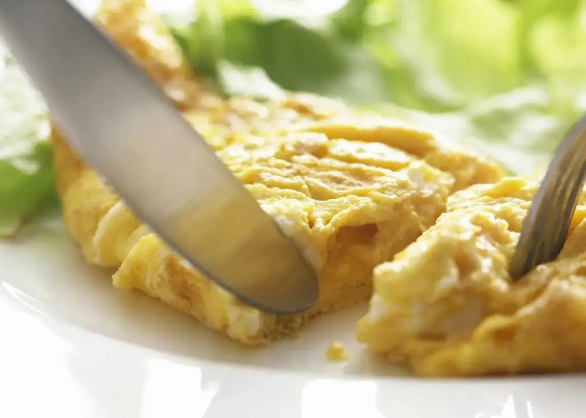 Una tortilla francesa esponjosa se corta con un cuchillo, lista para ser disfrutada con una guarnici&oacute;n de lechuga fresca.
