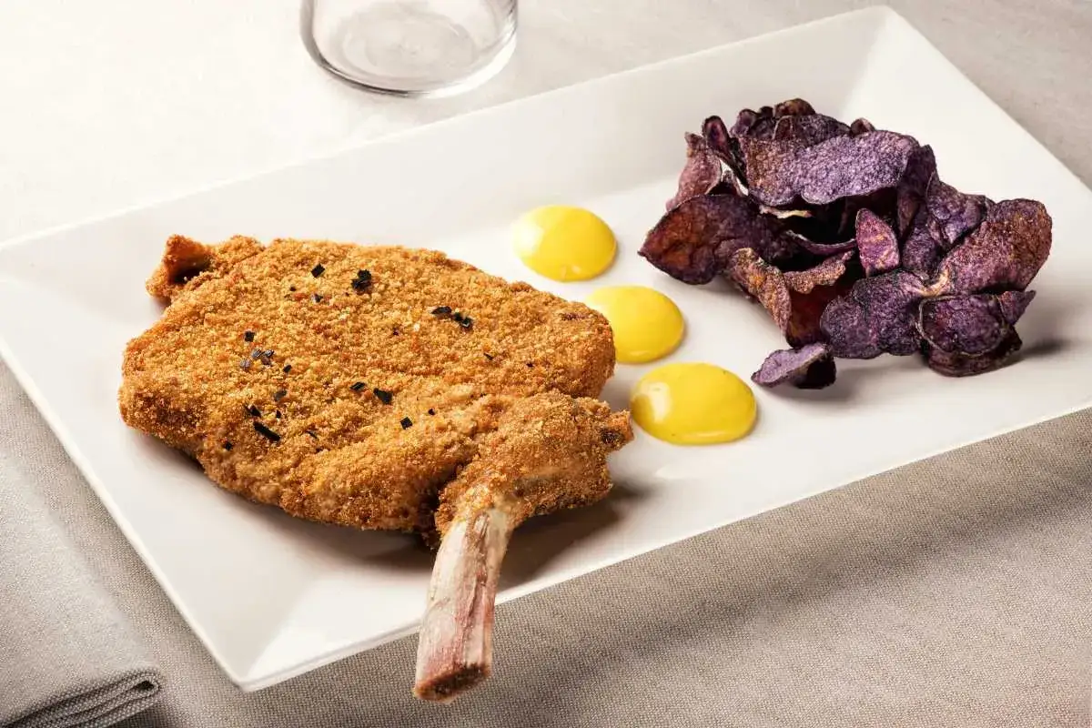 Un crujiente escalope de ternera con hueso, acompañado de patatas moradas y tres gotas de salsa amarilla.