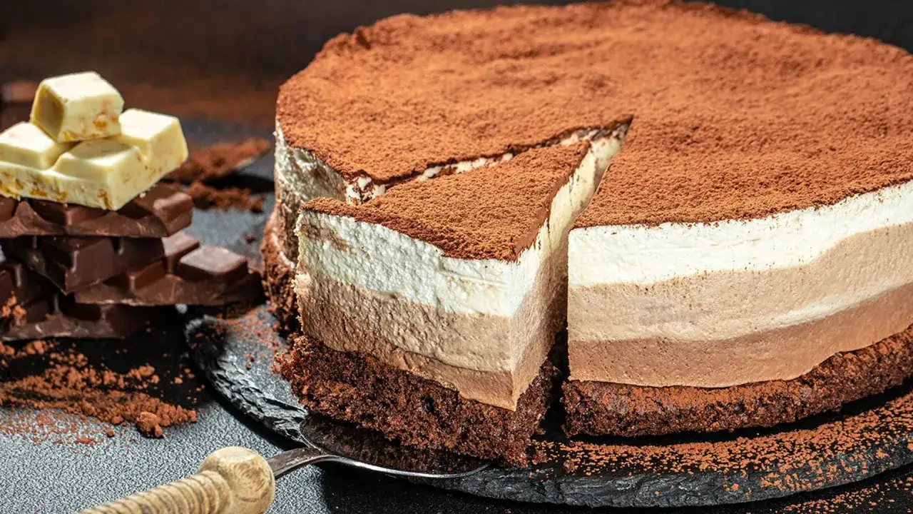 Deliciosa tarta de tres chocolates, con capas de mousse de chocolate blanco, con leche y negro, espolvoreada con cacao.